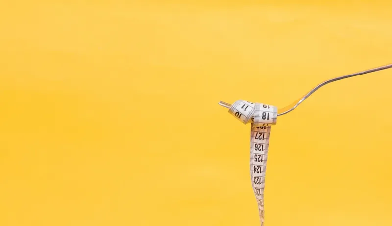 Tenedor de metal y cinta métrica blanca sobre un fondo amarillo.
