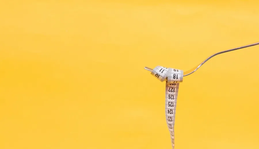 Tenedor de metal y cinta métrica blanca sobre un fondo amarillo.