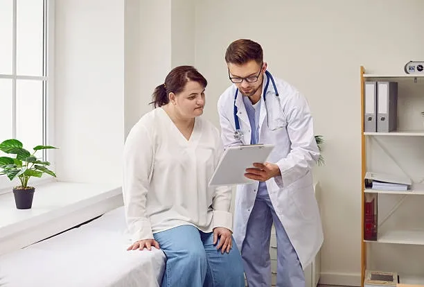 Médico mostrando una gráfica a un paciente durante una consulta de apoyo en un consultorio médico luminoso.