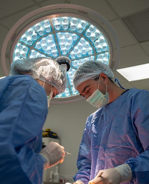 Two surgeons operate under bright lights in a sterile operating room.