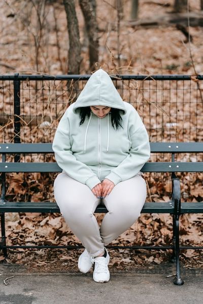 A woman in a hoodie sitting alone on a park bench
