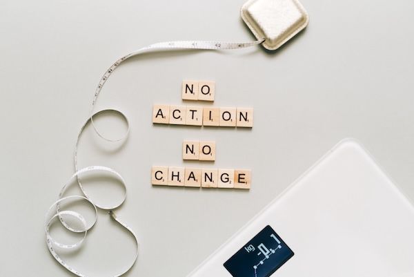 Bathroom scale, measuring tape, and letter tiles reading "No Action, No Change."