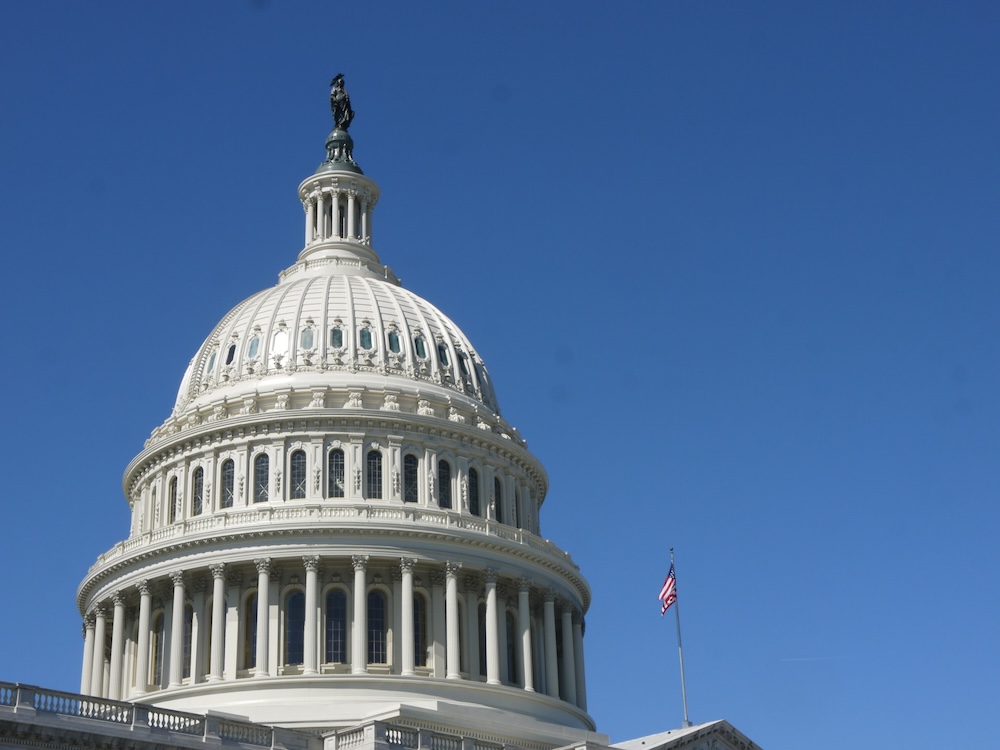 Image of the United States Capitol building with its iconic white dome and neoclassical columns set against a clear blue sky