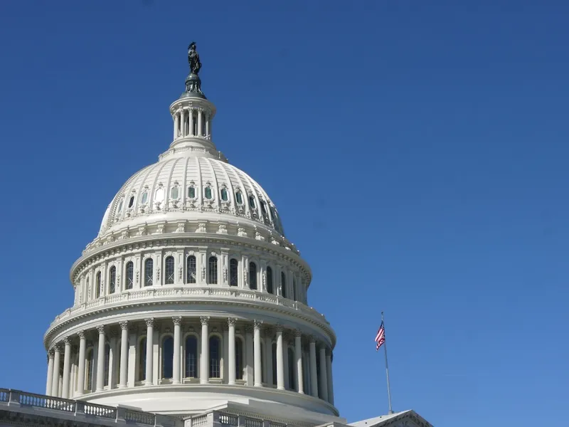 Image of the United States Capitol building with its iconic white dome and neoclassical columns set against a clear blue sky