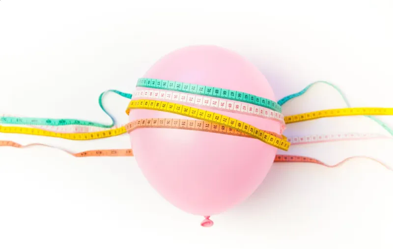 Un globo rosa envuelto con múltiples cintas métricas, simbolizando la pérdida de peso y la medición.